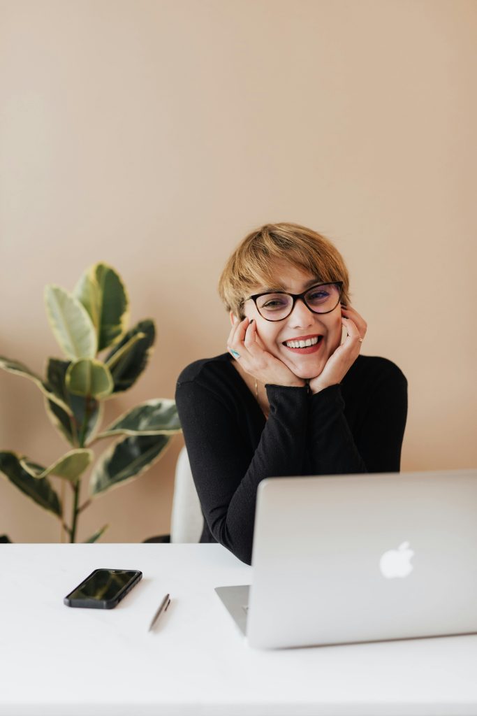 Cheerful woman smiling while sitting at table with laptop // Healthier Pets Today