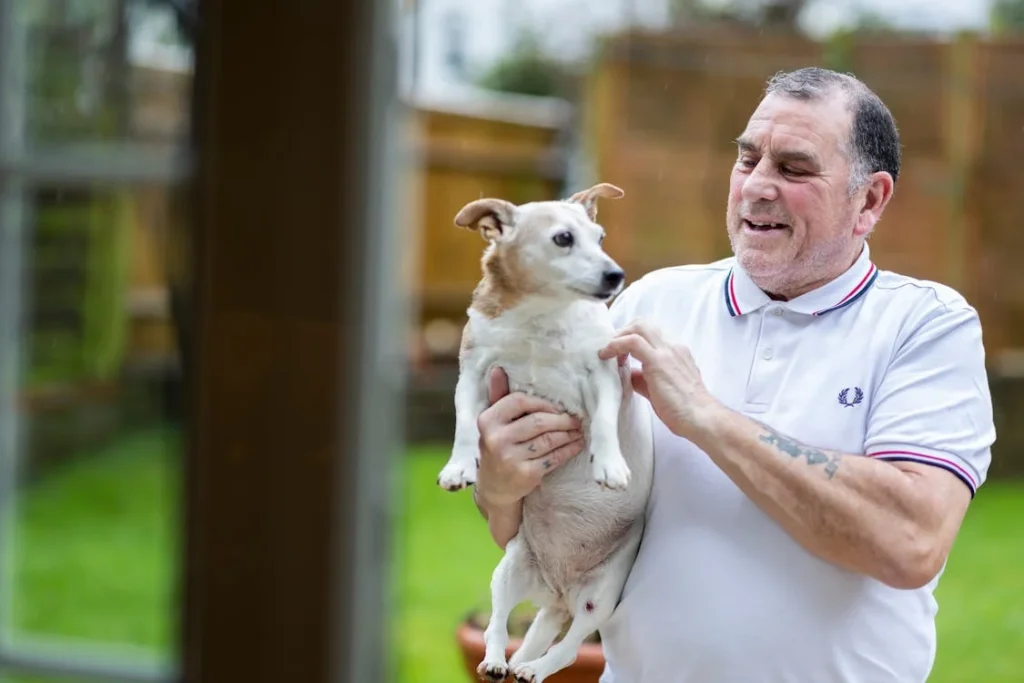 Elderly Man in Polo Shirt Holding Dog in Hands // Healthier Pets Today