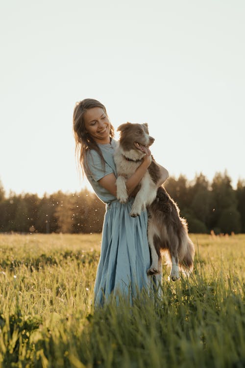 Woman in Blue Dress Standing on Green Grass Field With White and Black Long Coated Dog // Healthier Pets Today