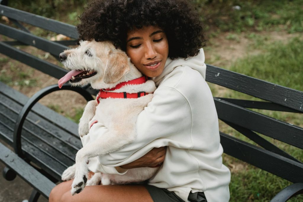 woman hugging her small white dog, black bench, grass // Healthier Pets Today
