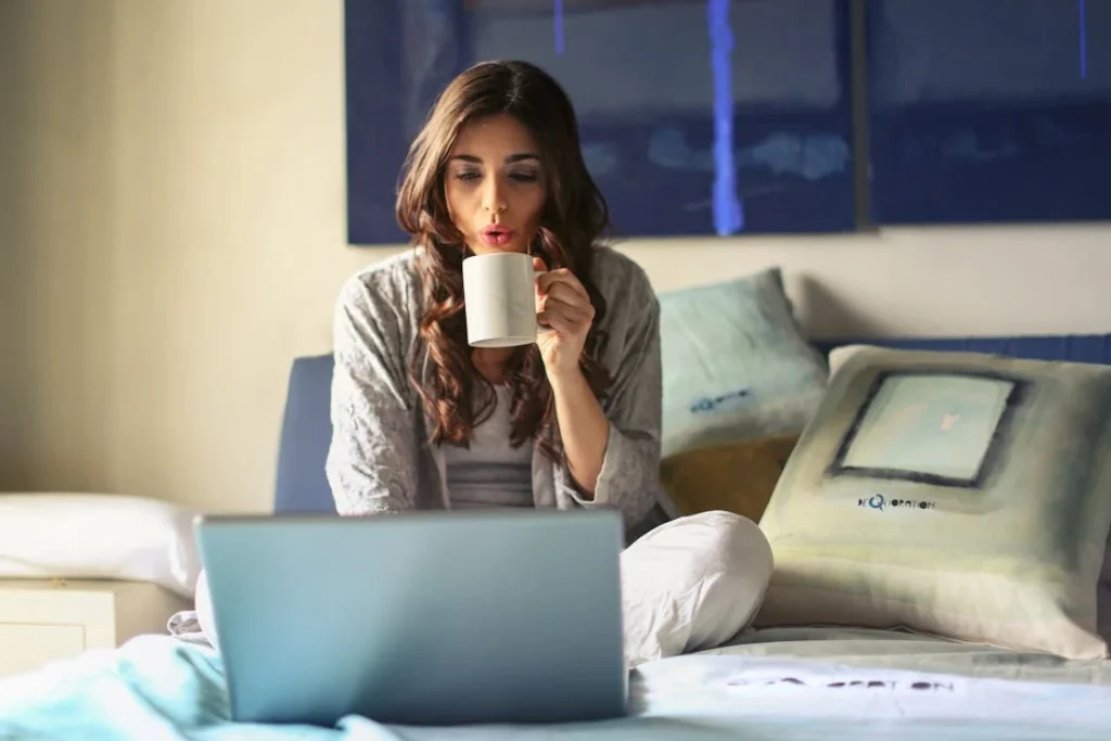 Woman in Grey Jacket Sits on Bed Uses Grey Laptop // Healthier Pets Today