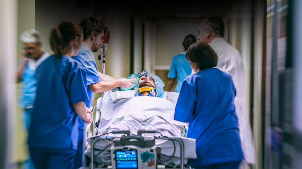 Patient getting transported to emergency room to get help, medical professionals around bed in hall way // Healthier Pets Today